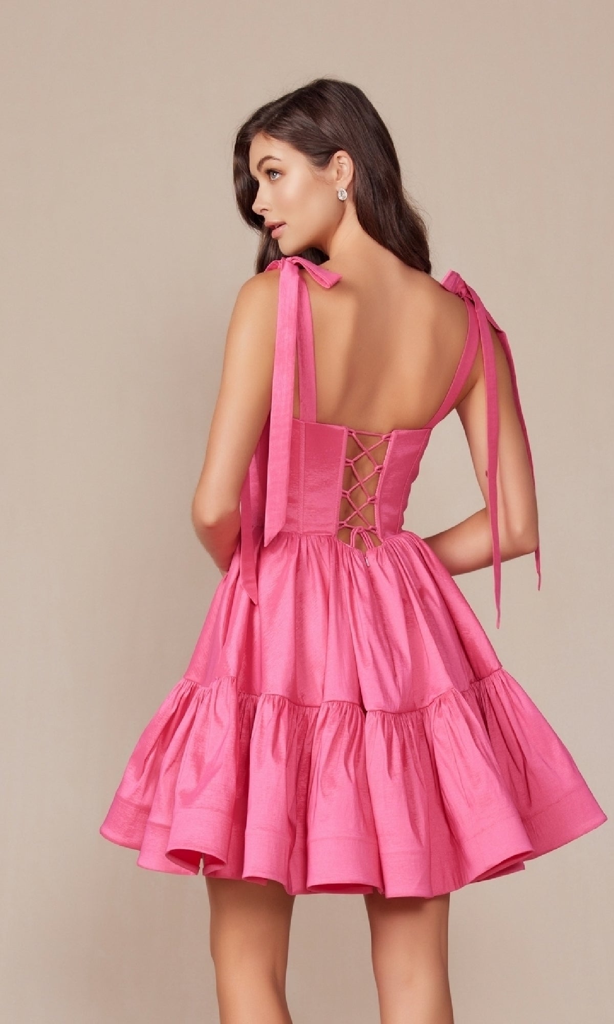 Woman modeling the Shoulder-Tie Short Lace-Up A-Line Hoco Dress T869, a sleeveless, backless pink dress with ribbon shoulder ties and lace-up back, shown against a neutral background.